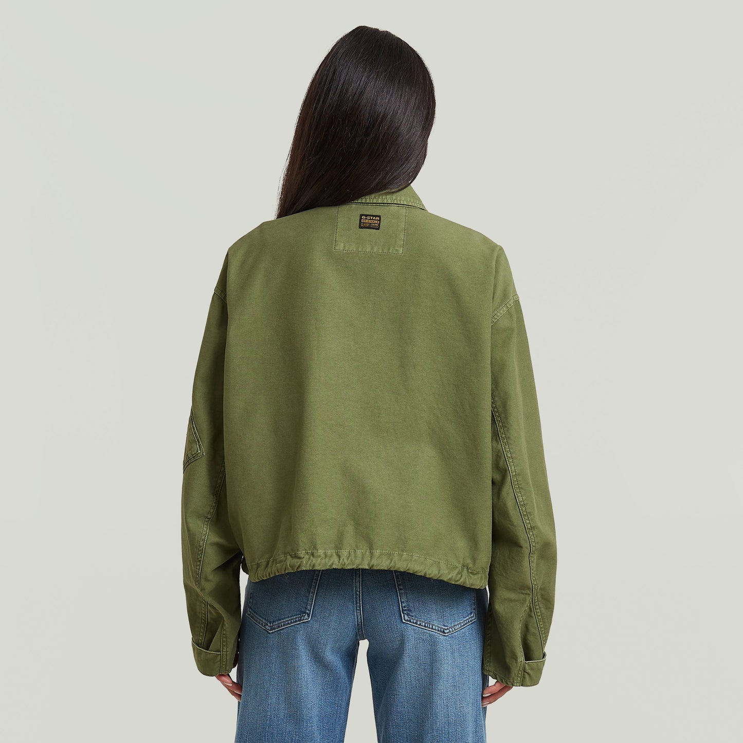 Mujer usando una chaqueta oversized cropped verde desde la parte trasera, mostrando el diseño relajado y el bajo elástico.