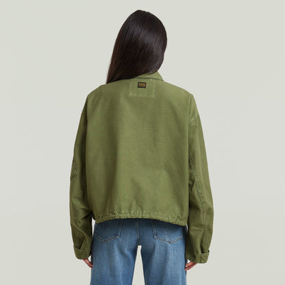 Mujer usando una chaqueta oversized cropped verde desde la parte trasera, mostrando el diseño relajado y el bajo elástico.