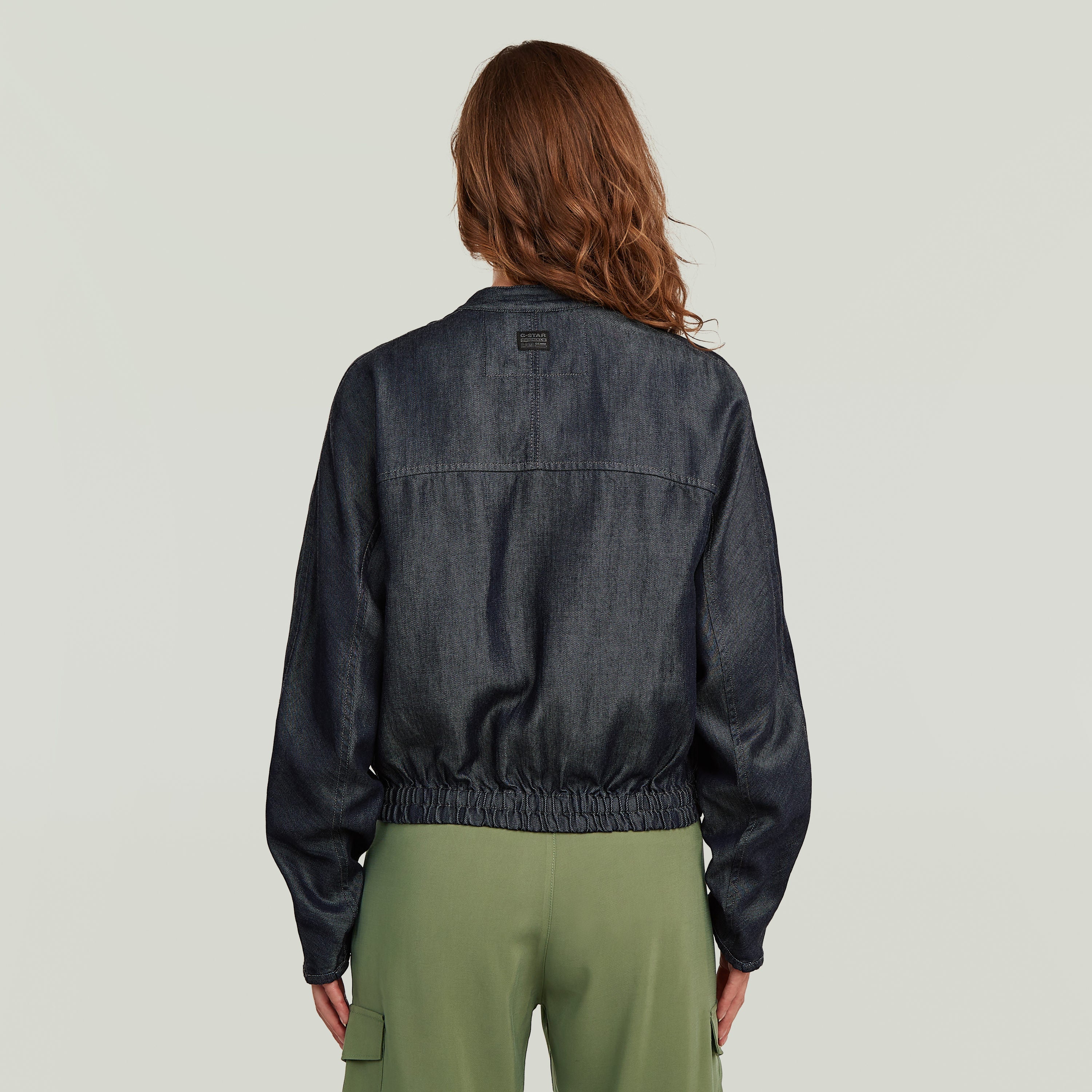 Mujer vista de espaldas usando una cazadora bomber summer ligera de denim oscuro.