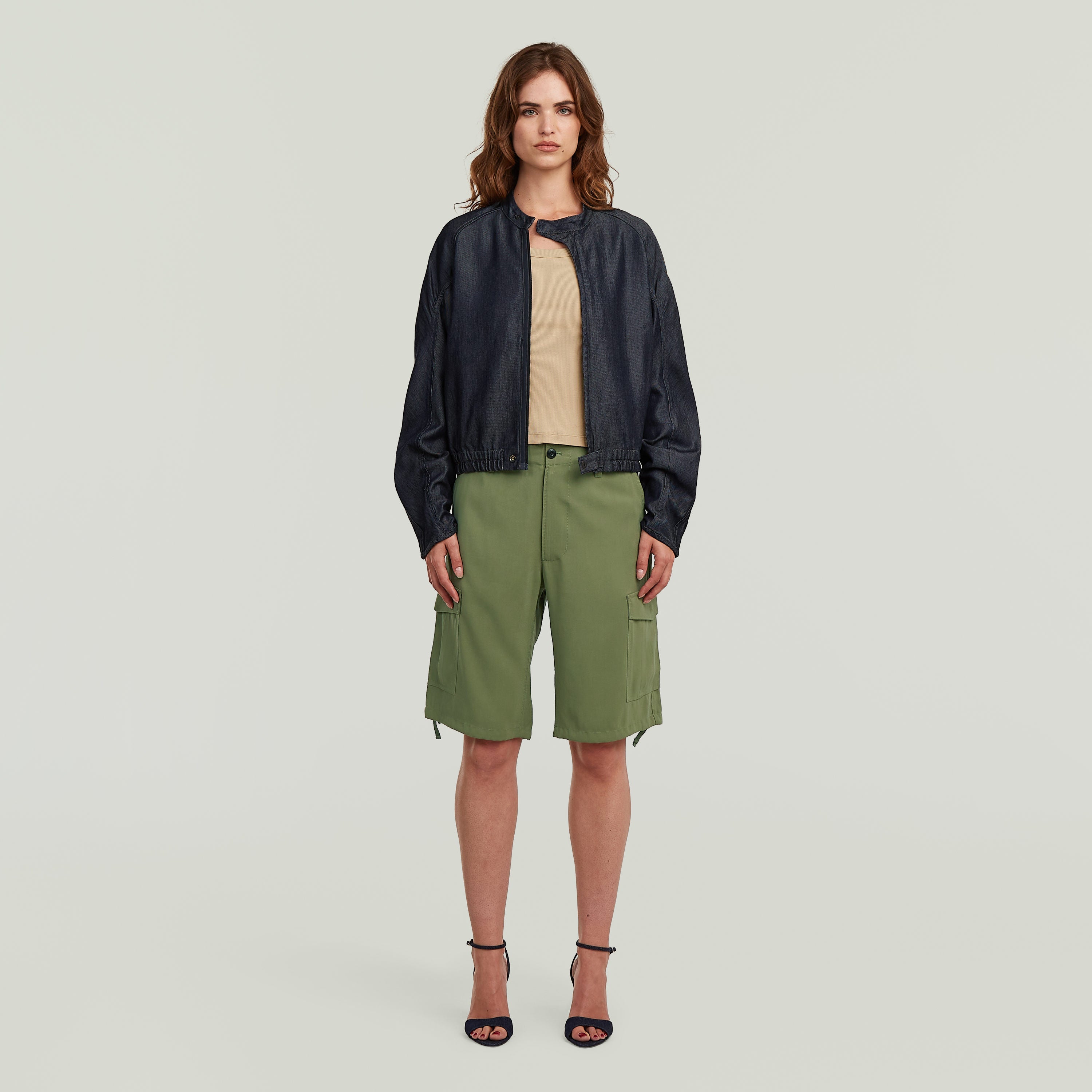 Modelo usando una cazadora bomber summer ligera, con corte regular, en denim oscuro y shorts verdes.