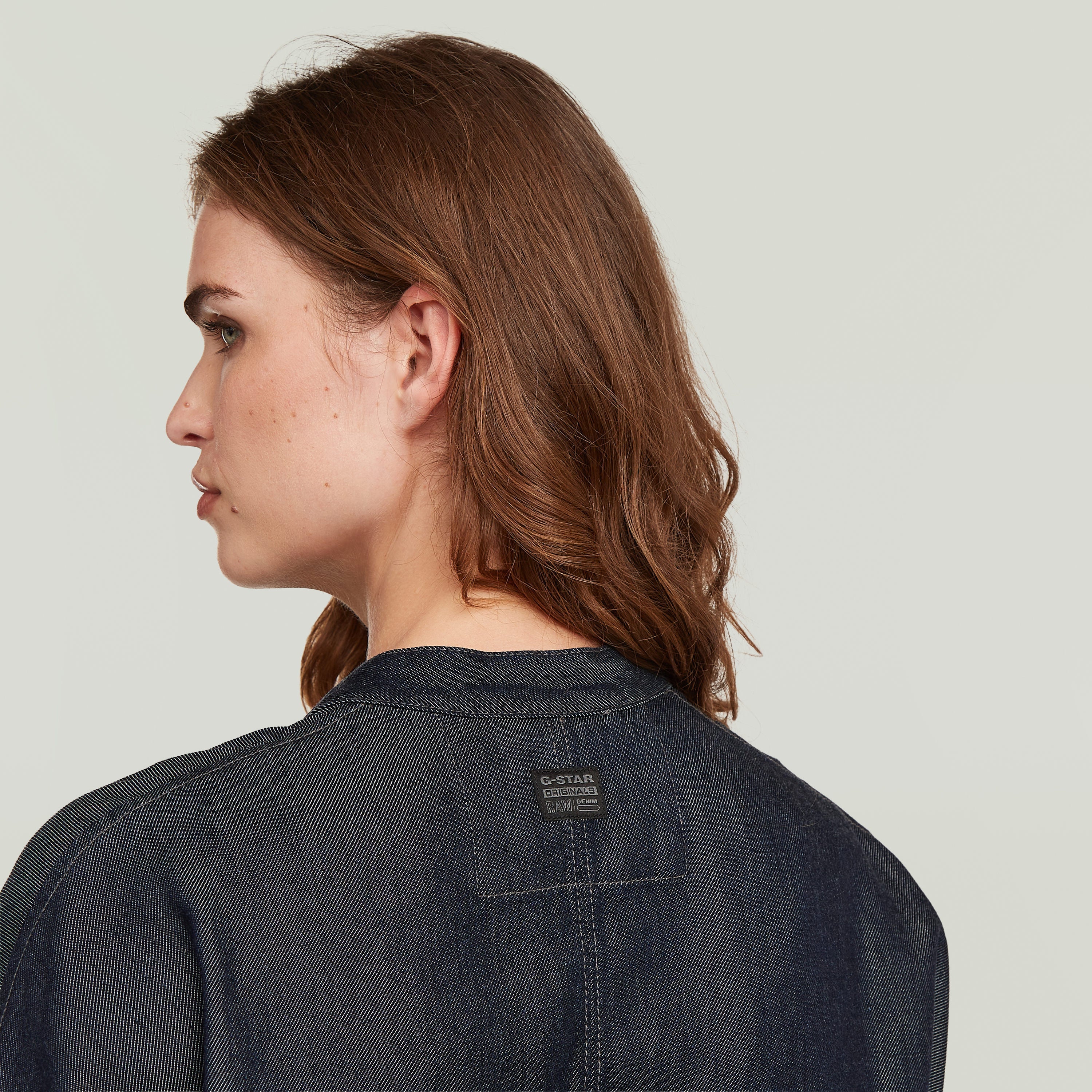 mujer con cazadora bomber summer ligera de denim oscuro, vista trasera mostrando etiqueta G-STAR