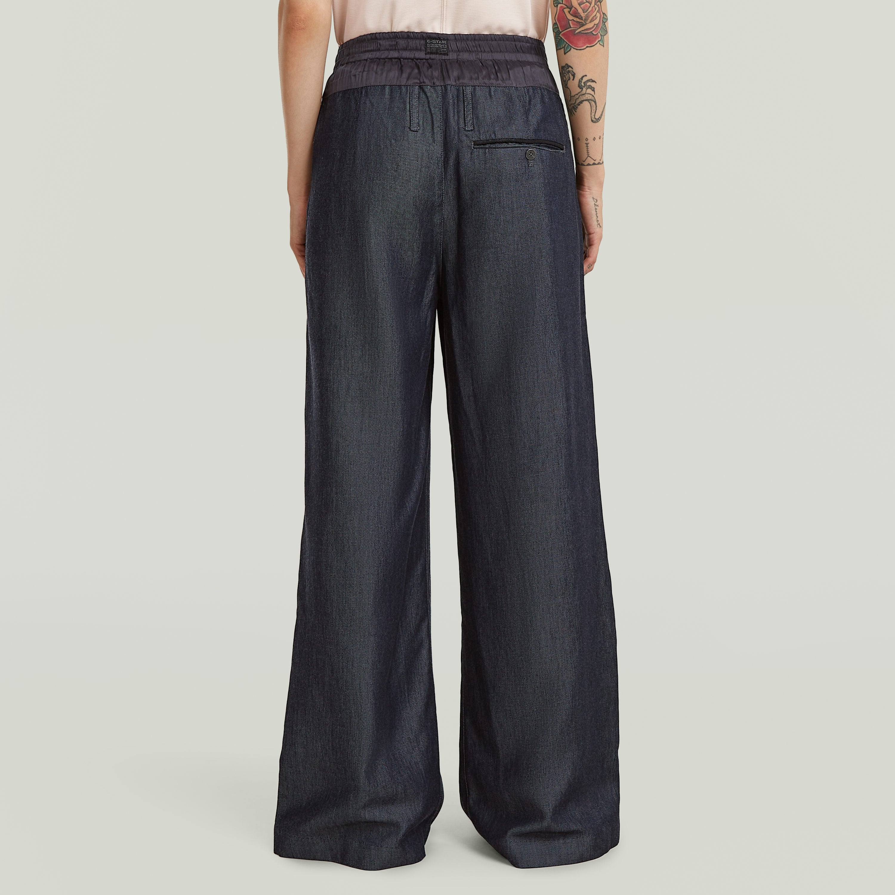 Vista trasera de pantalones fluidos de denim ligero en índigo oscuro con corte holgado y talle alto.