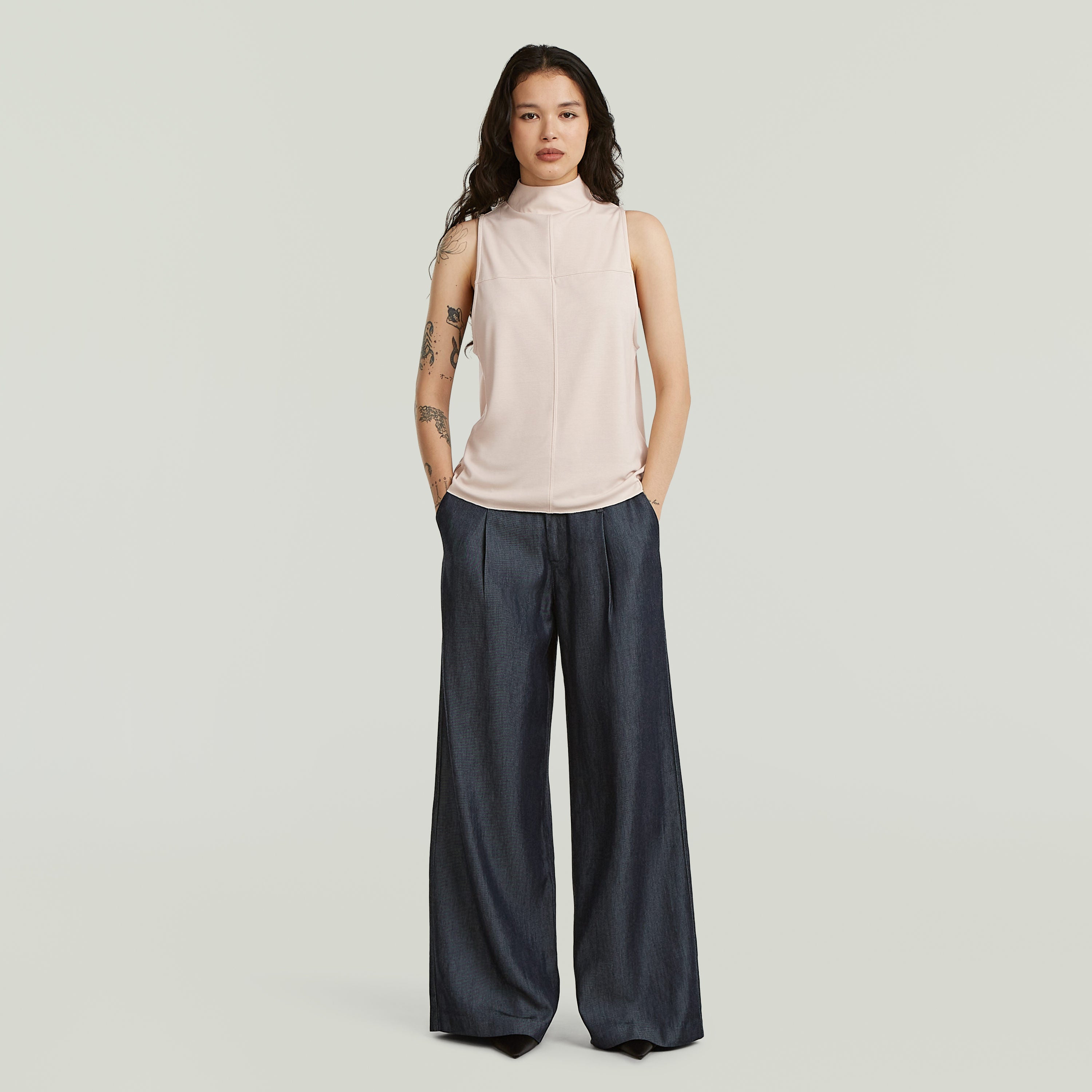 Mujer usando pantalones fluidos de denim ligero en índigo oscuro y top sin mangas elegante.