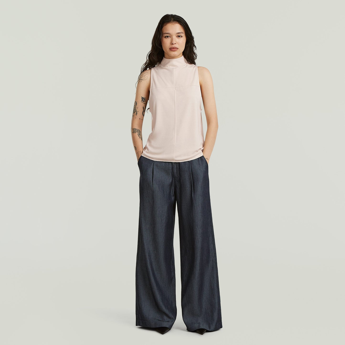 Mujer usando pantalones fluidos de denim ligero en índigo oscuro y top sin mangas elegante.
