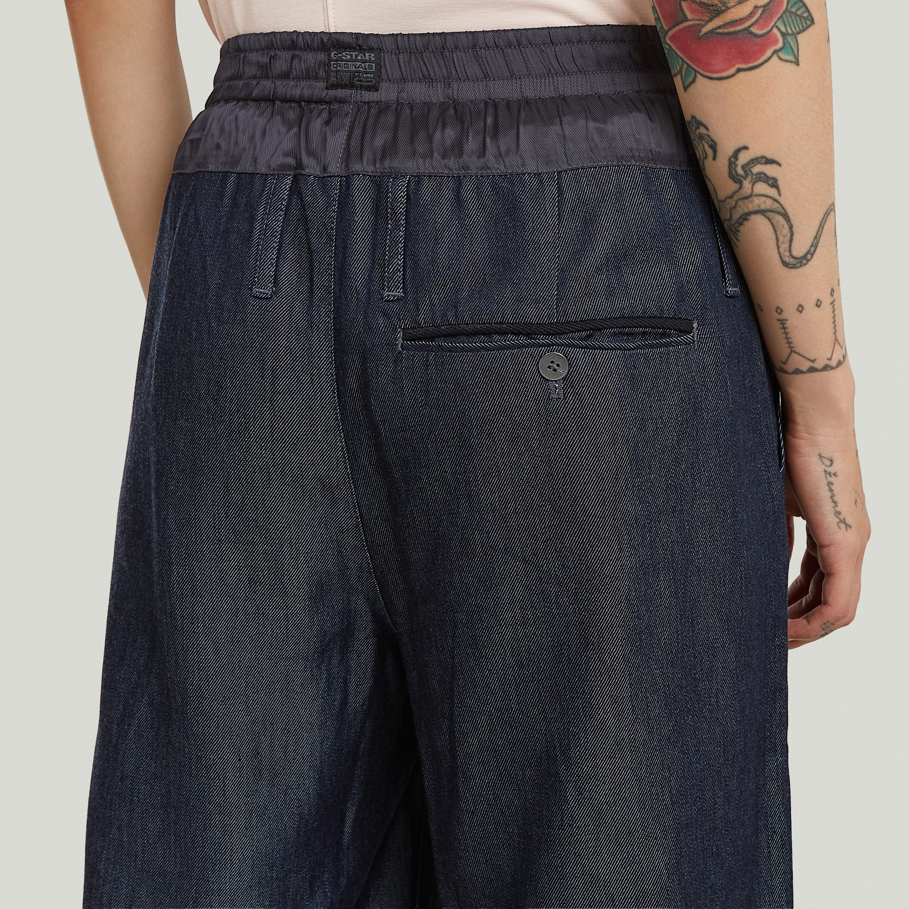 pantalones fluidos de denim ligero, vista trasera con detalles de botón y bolsillos, diseño elegante y cómodo.