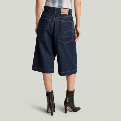 Mujer usando jorts de algodón reciclado con borde limpio, vista trasera, color azul oscuro.