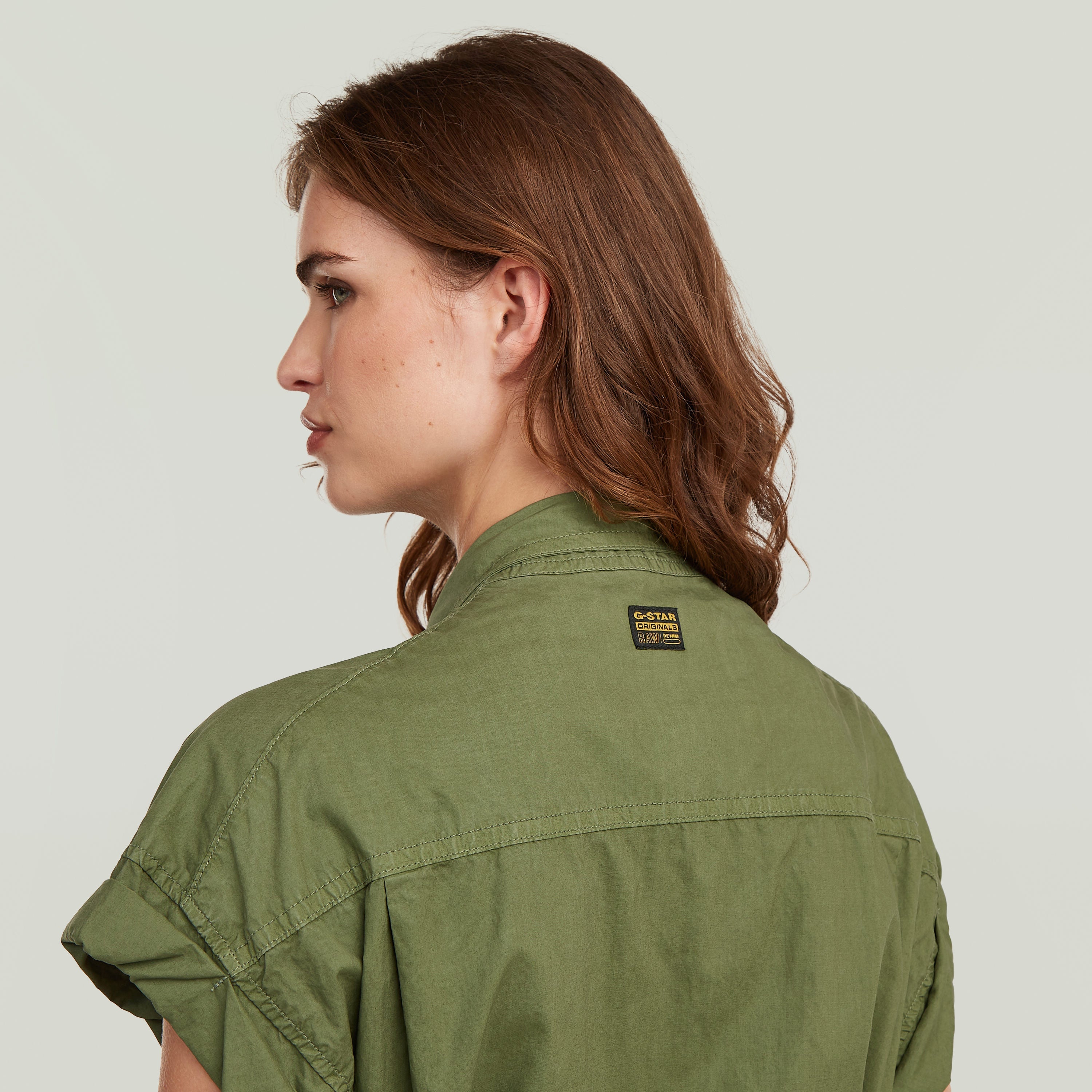 Woman wearing a lightweight green shirt with rolled short sleeves, showcasing a casual back view.