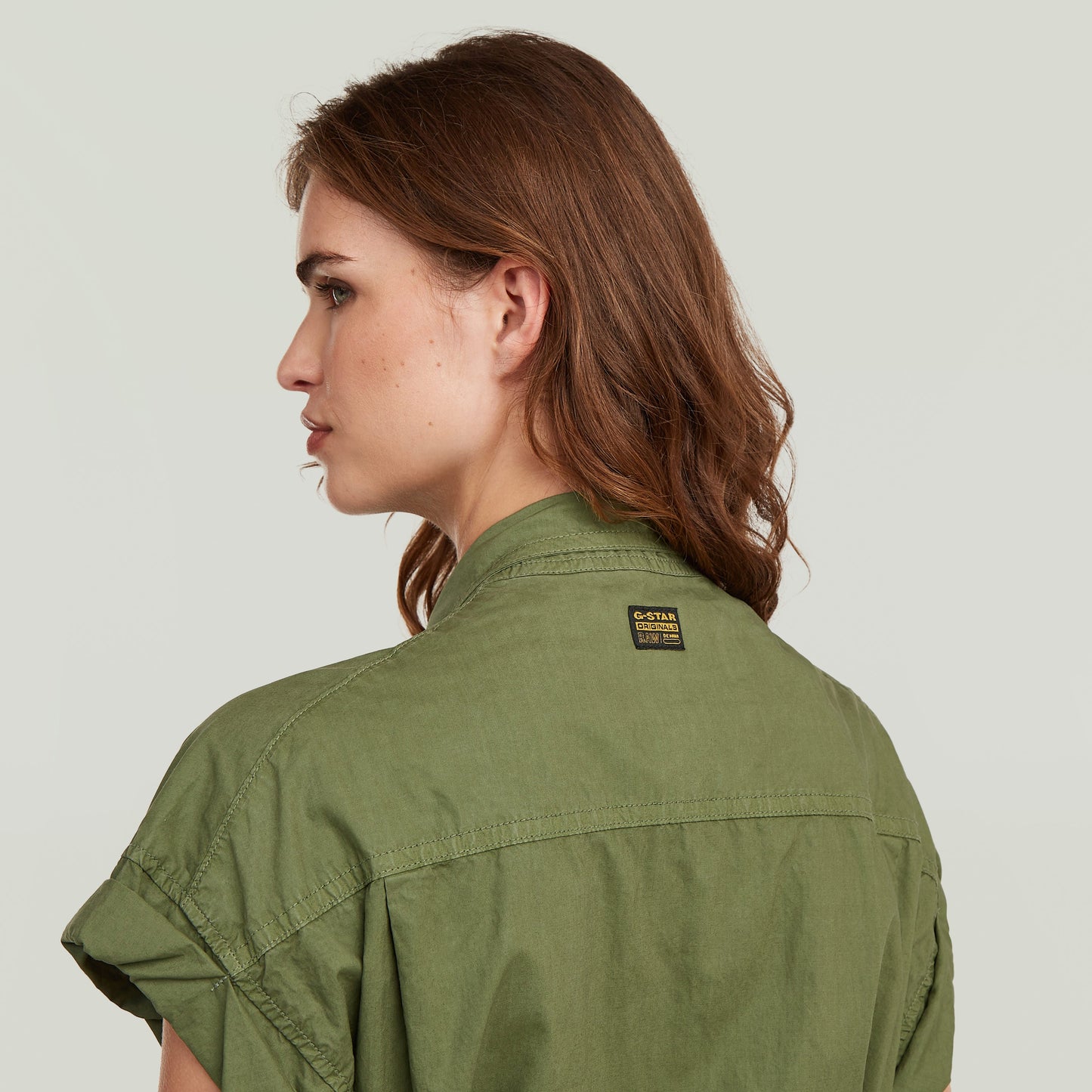 Woman wearing a lightweight green shirt with rolled short sleeves, showcasing a casual back view.