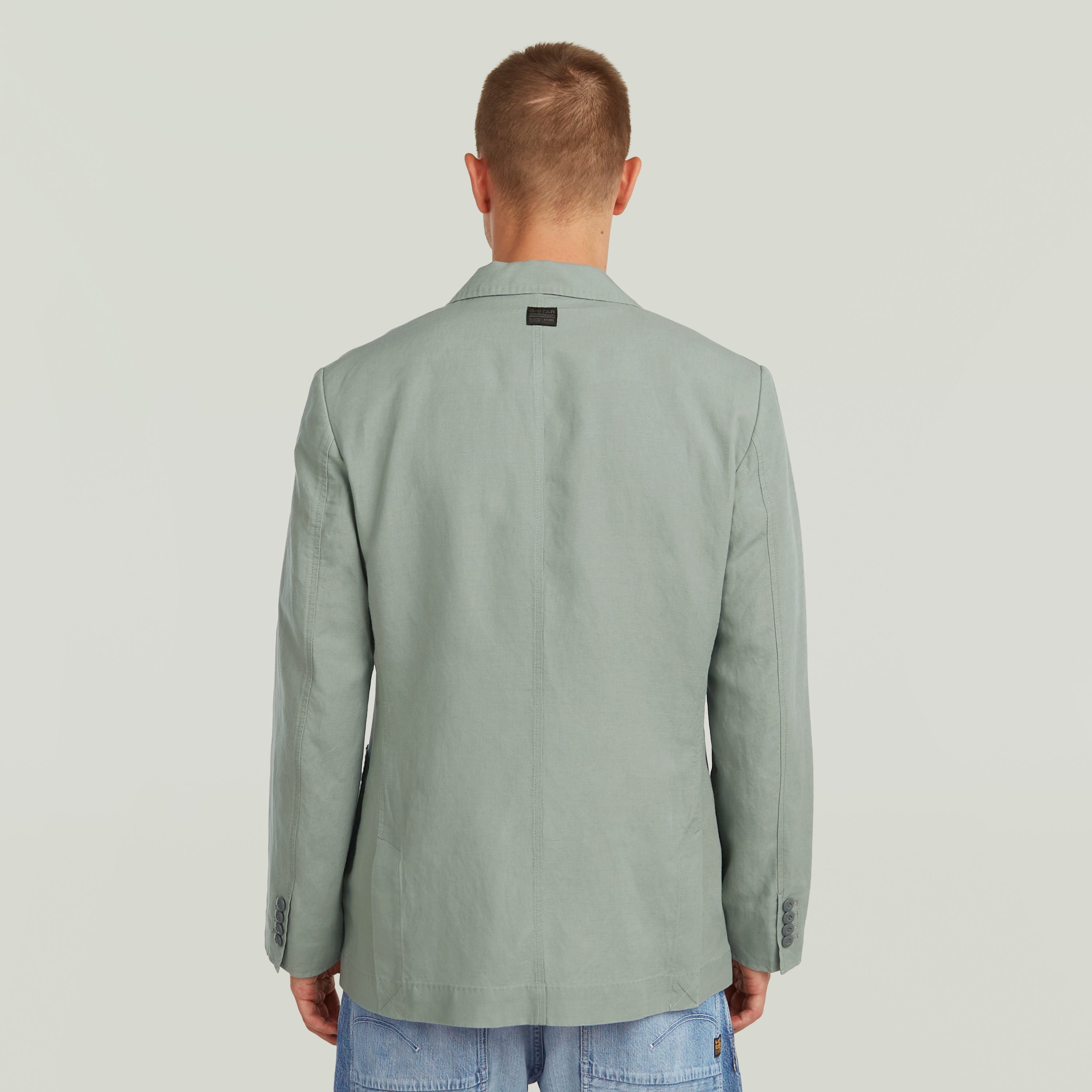 Back view of a man wearing a lightweight green blazer, showcasing its refined design and breathable fabric.