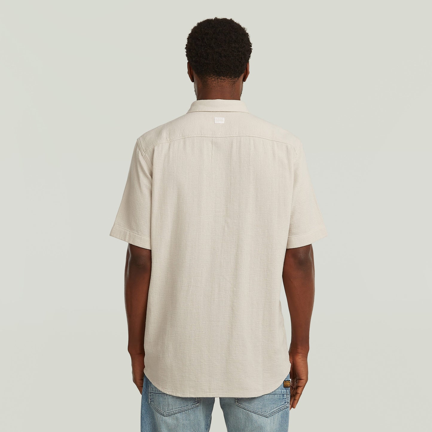 Hombre de espaldas vistiendo una camisa one pocket regular de color blanco con diseño clásico y moderno.