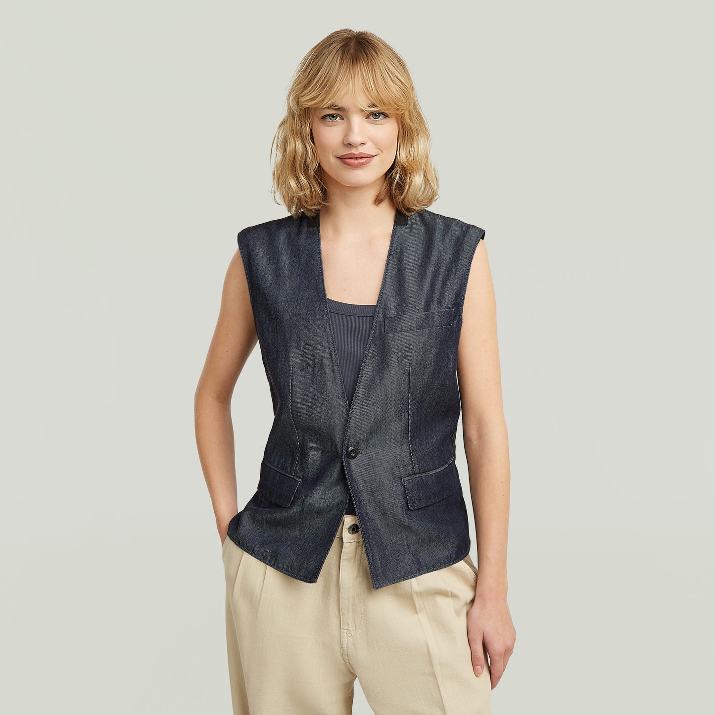 Modelo luciendo un ligero chaleco blazer de denim en índigo oscuro con diseño sin mangas.