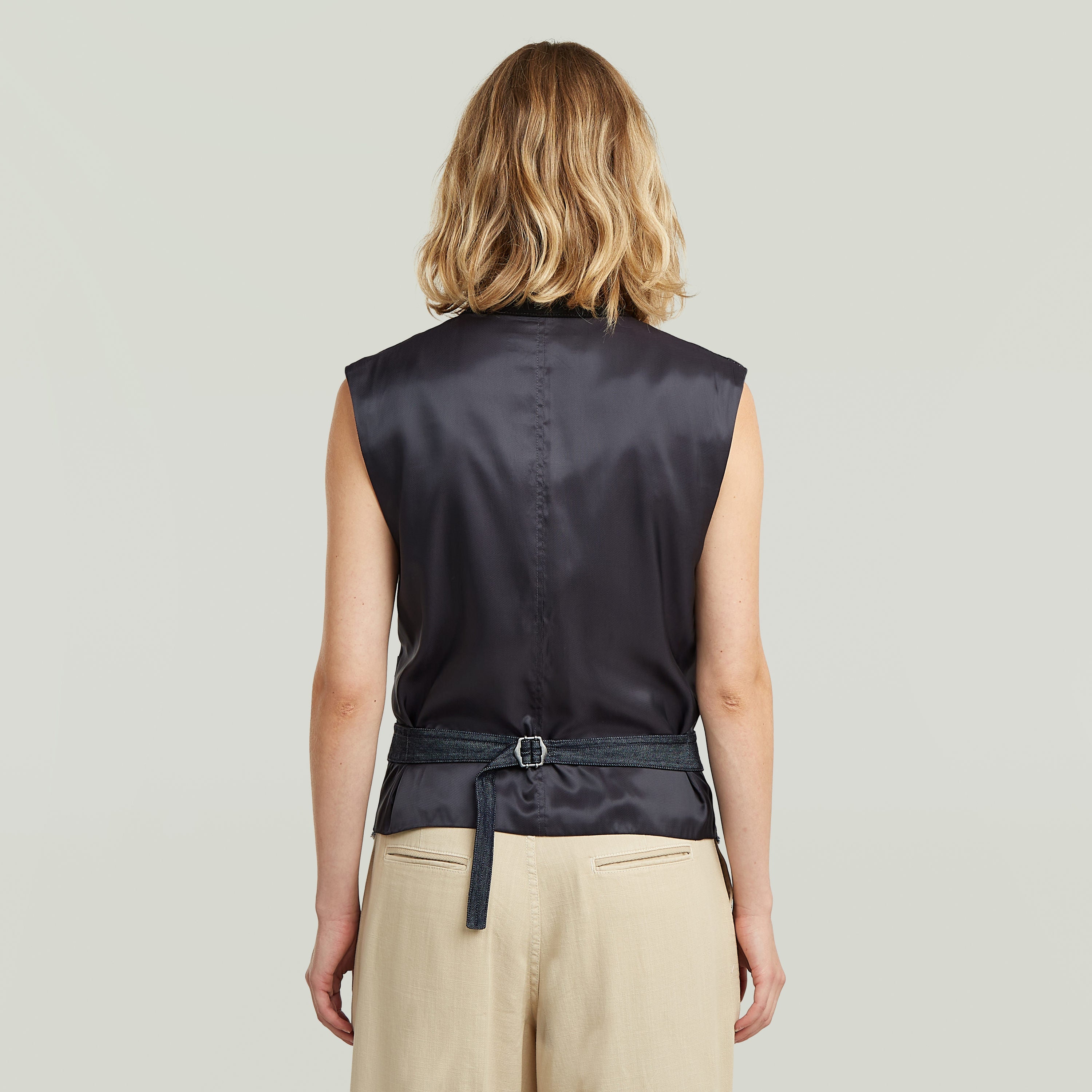 Mujer de espaldas vistiendo un ligero chaleco blazer de denim, con diseño sin mangas y cinturón ajustable.
