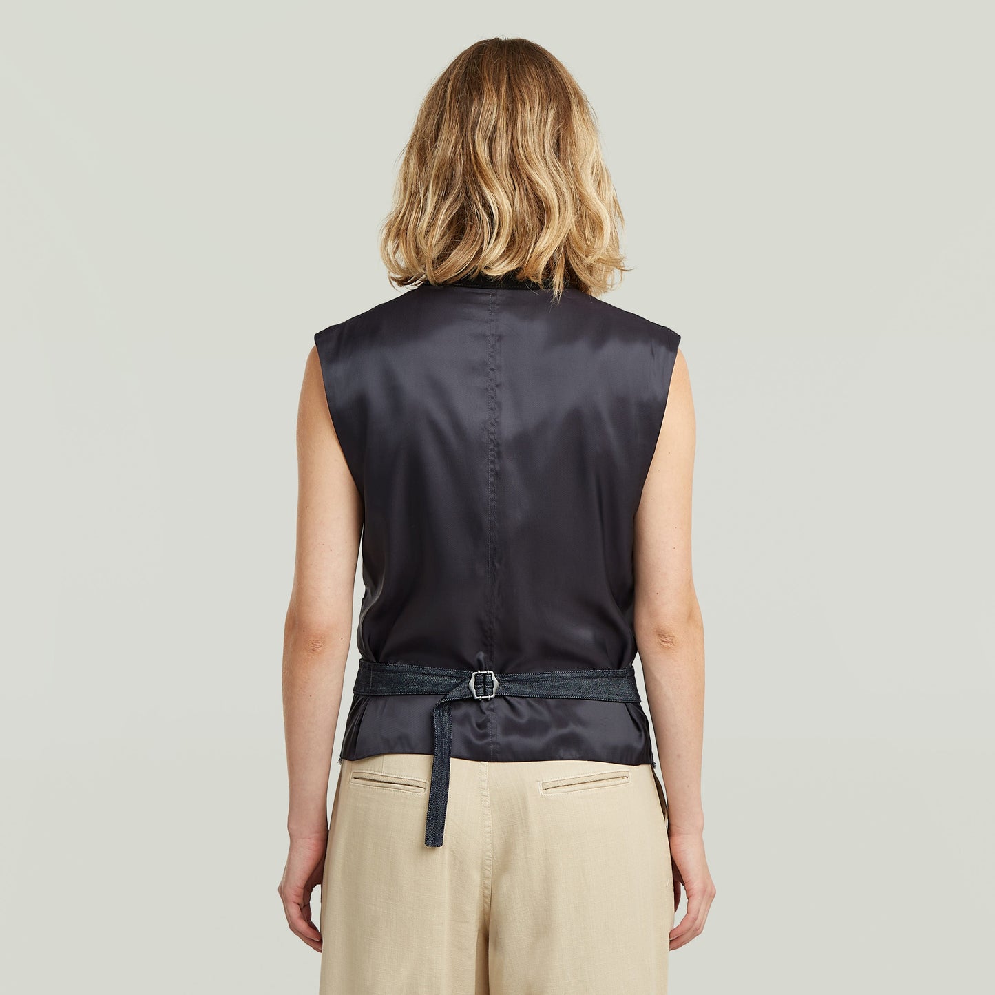 Mujer de espaldas vistiendo un ligero chaleco blazer de denim, con diseño sin mangas y cinturón ajustable.