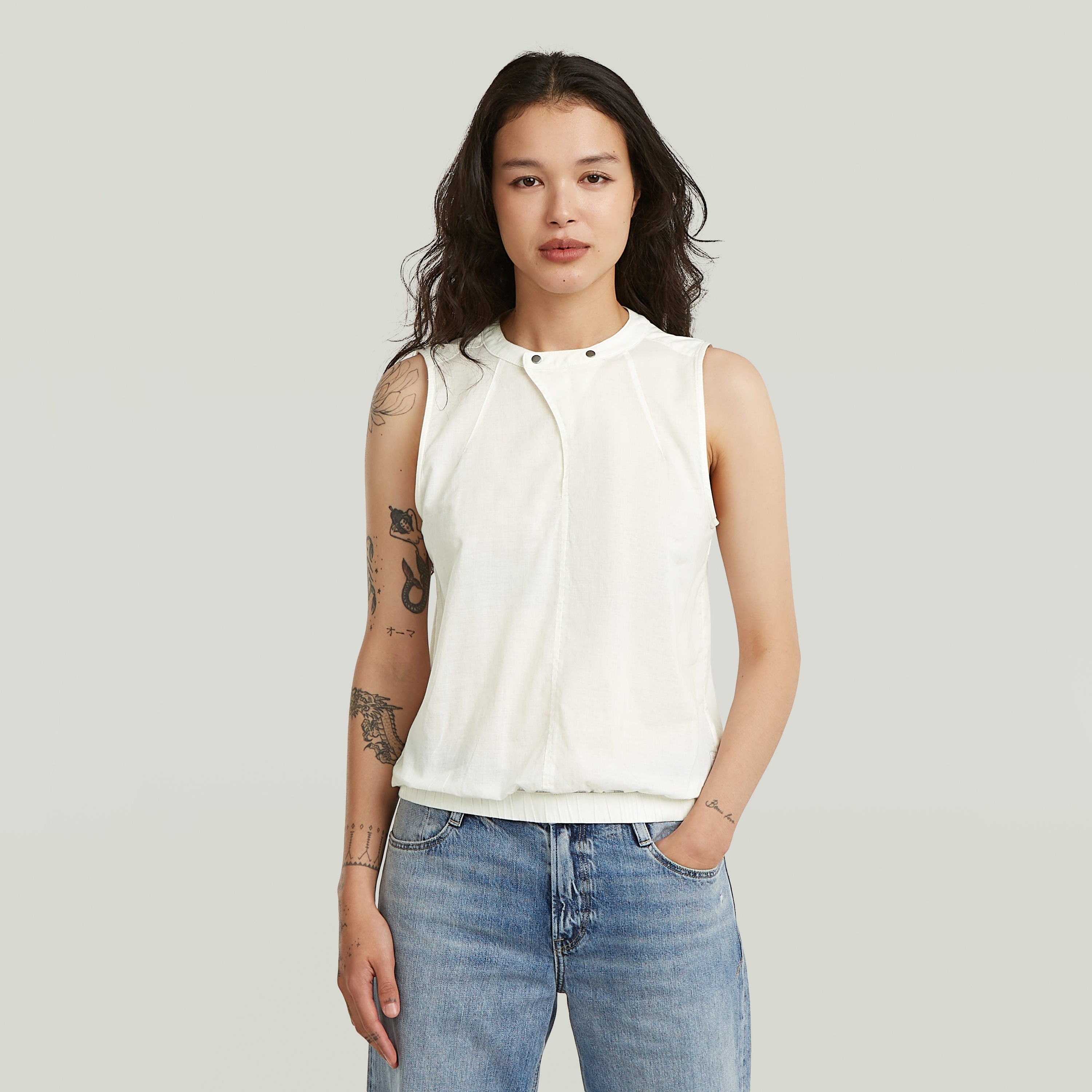 Mujer con camiseta sin mangas de cuello alzado en color blanco, mostrando un estilo moderno y fresco, sleeveless high-neck cotton t-shirt.