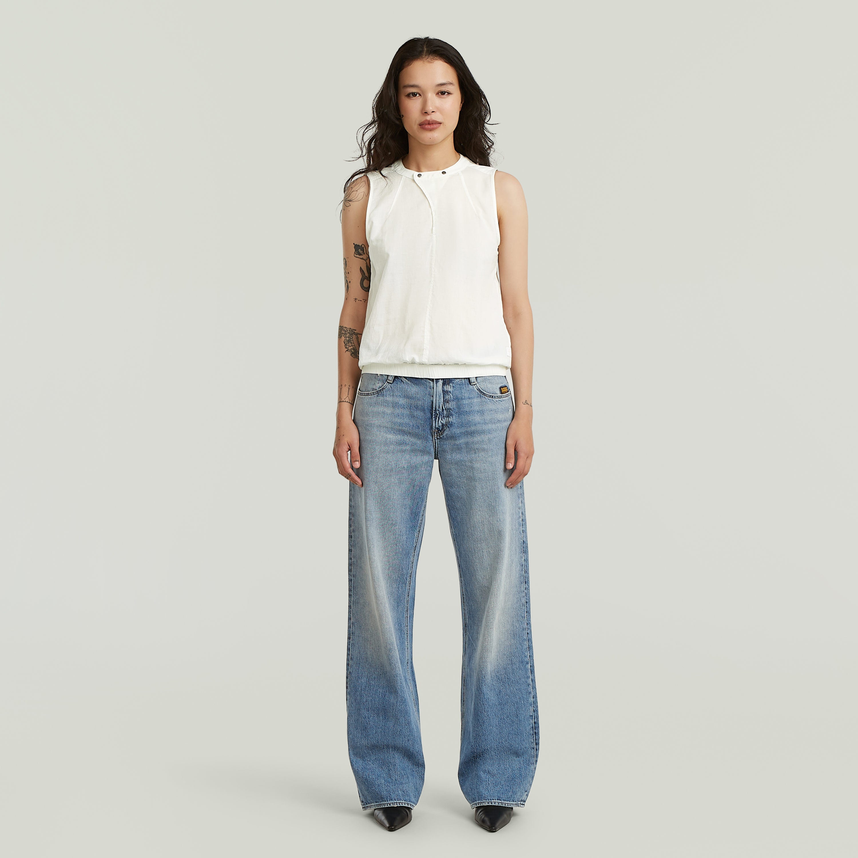 Camiseta sin mangas de alto cuello en algodón blanco, combinada con jeans de corte amplio.