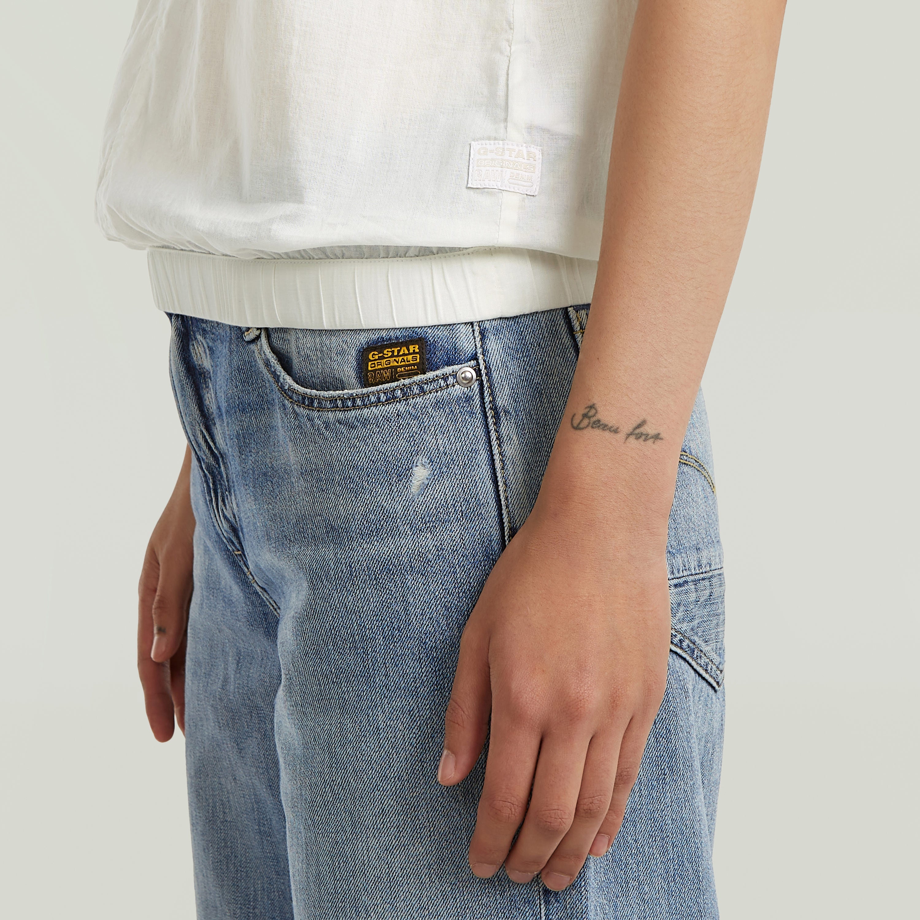 sleeveless high-neck cotton t-shirt paired with blue denim jeans, showcasing modern casual style.