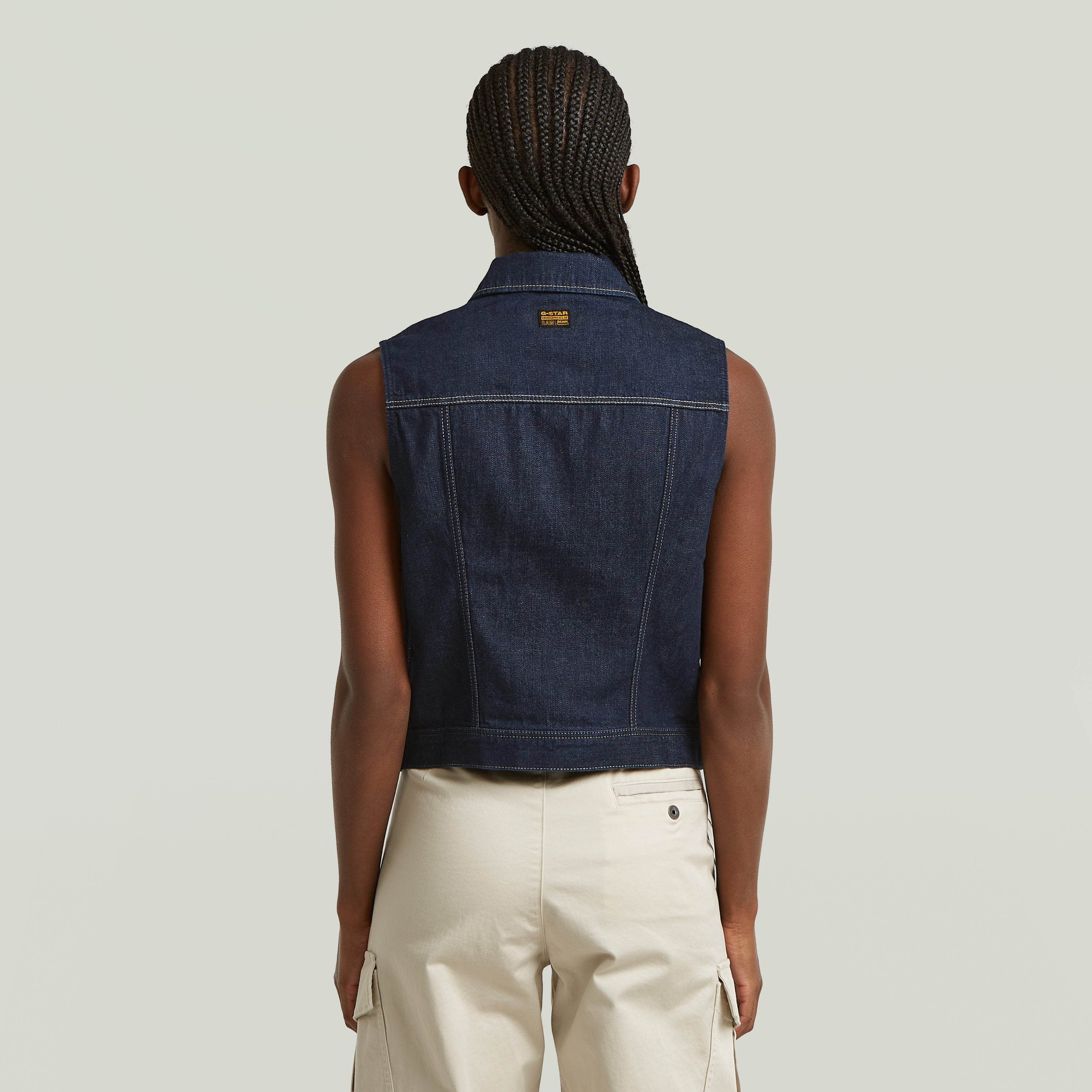 Back view of a stylish model wearing a slim fit denim vest in dark blue, showcasing modern design and structure.