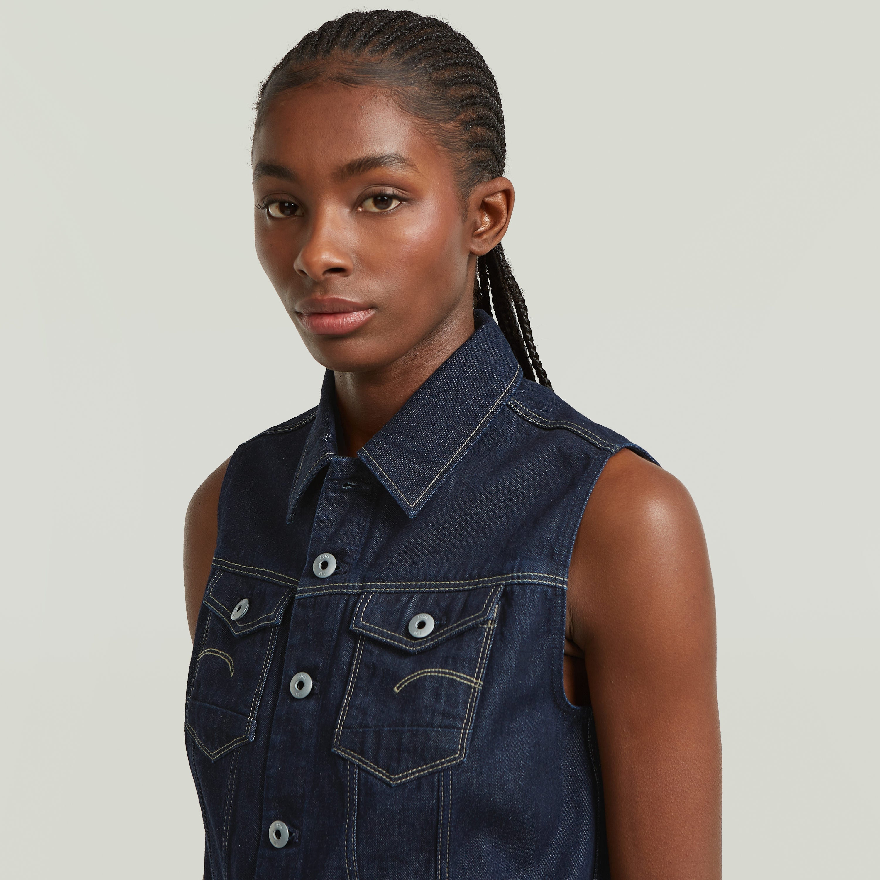 Close-up of a model wearing a slim fit denim vest with a shirt collar and button closure.