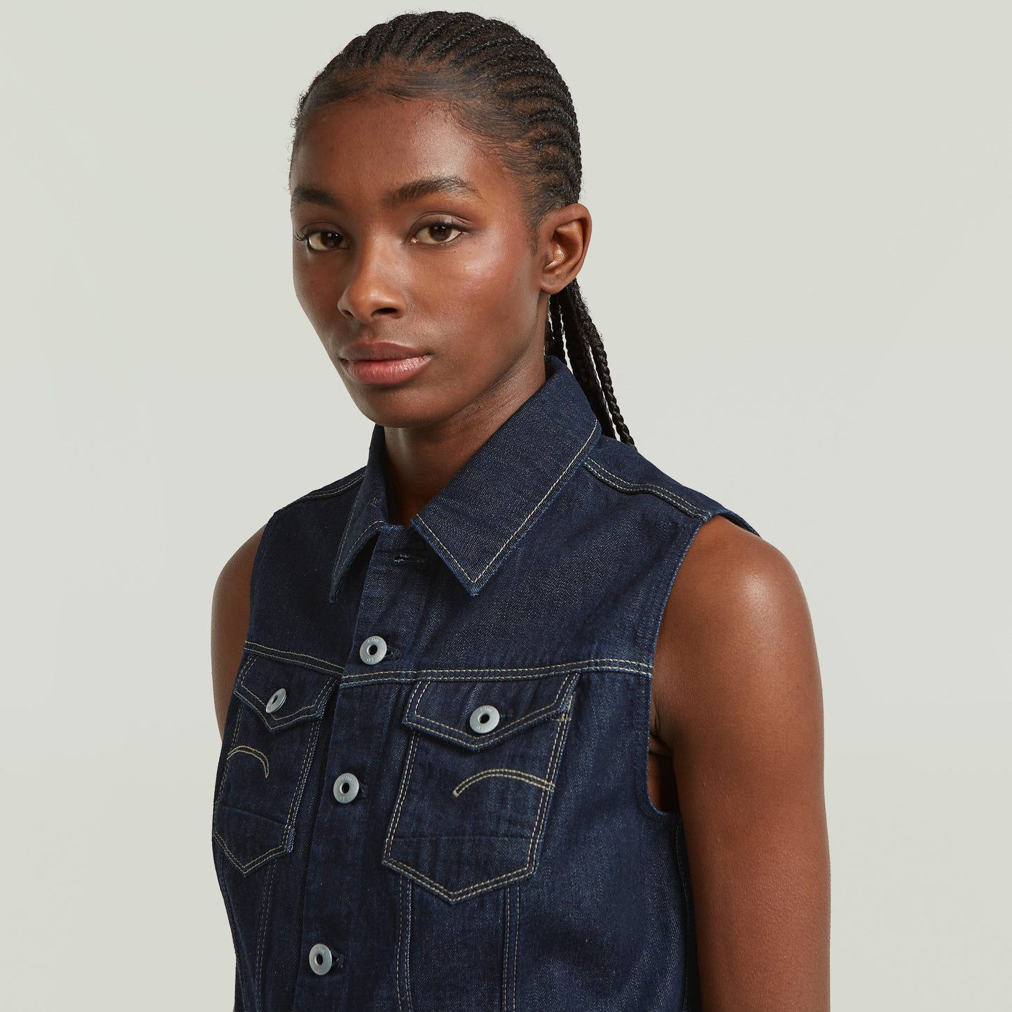 Close-up of a model wearing a slim fit denim vest with a shirt collar and button closure.