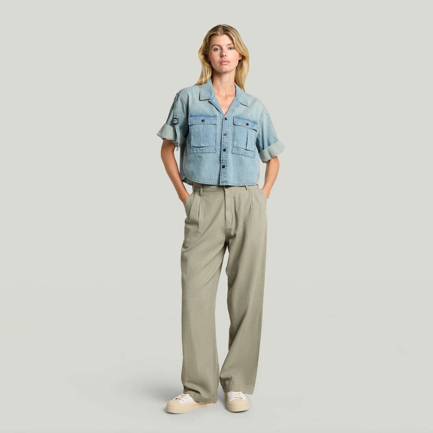 Modelo usando pantalones pleated chino en color verde con camisa de mezclilla, estilo atemporal y relajado.