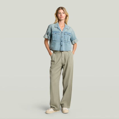 Modelo usando pantalones pleated chino en color verde con camisa de mezclilla, estilo atemporal y relajado.