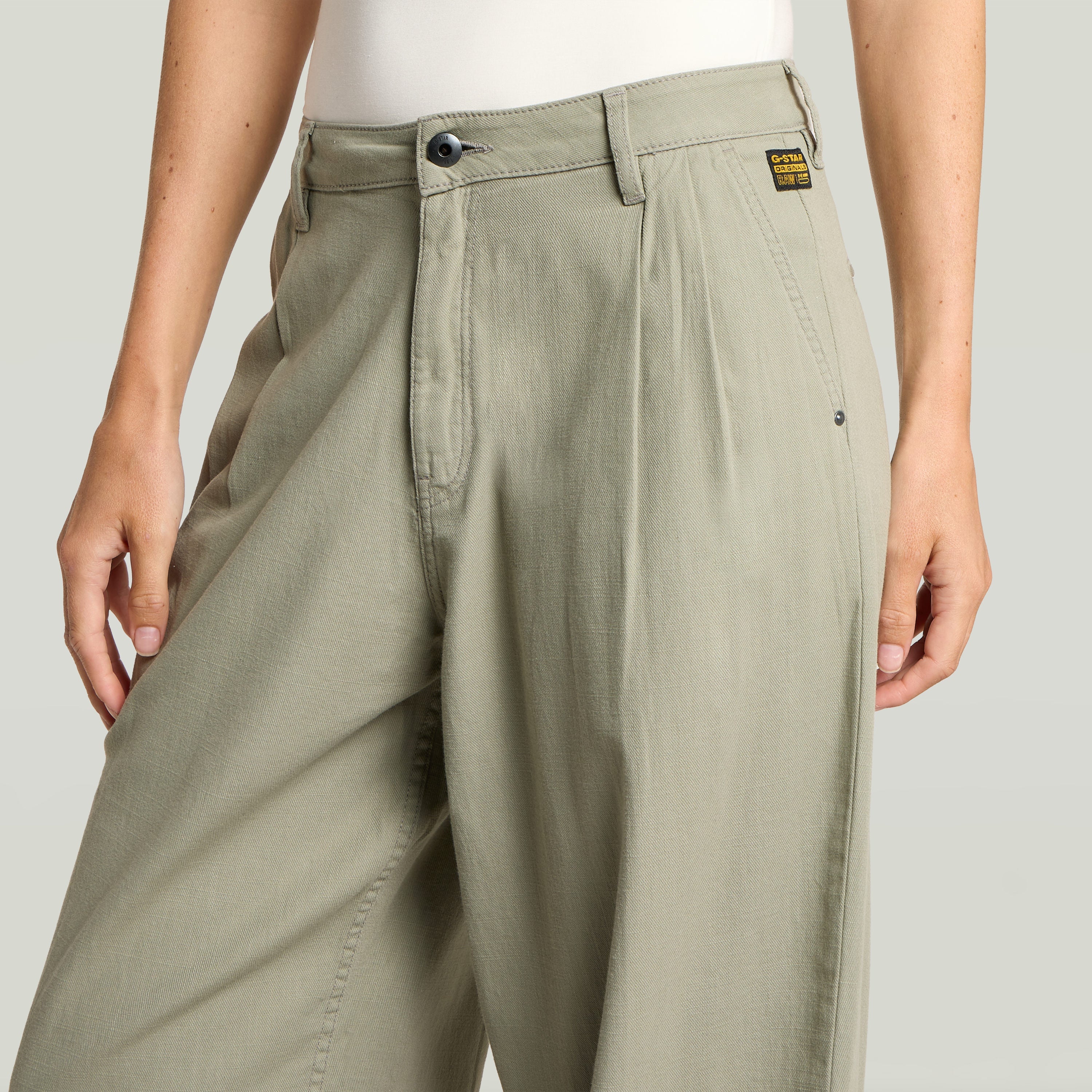 Primer plano de pantalones pleated chino pants en color verde con detalles plisados y cierre de botón.