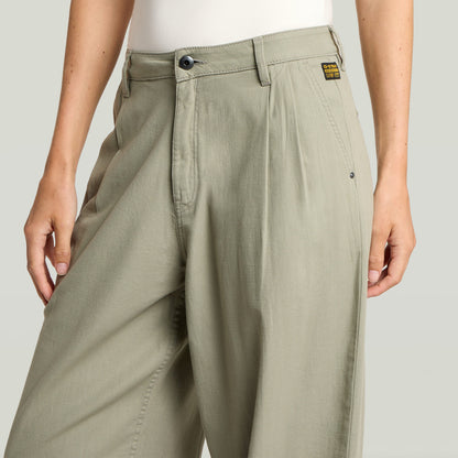 Primer plano de pantalones pleated chino pants en color verde con detalles plisados y cierre de botón.