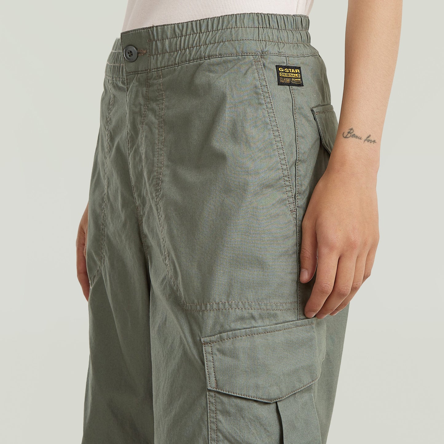 Dettaglio dei pantaloni wide leg cargo con tasche laterali e chiusura bottone in colore verde.
