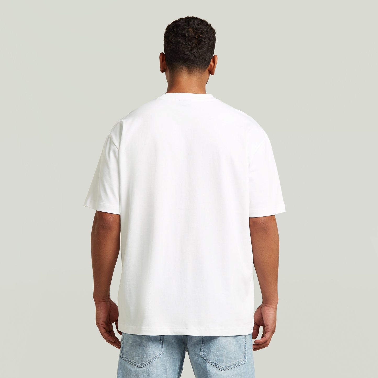 Model wearing a white relaxed graphic t-shirt, viewed from the back, showcasing the relaxed fit and comfortable design.