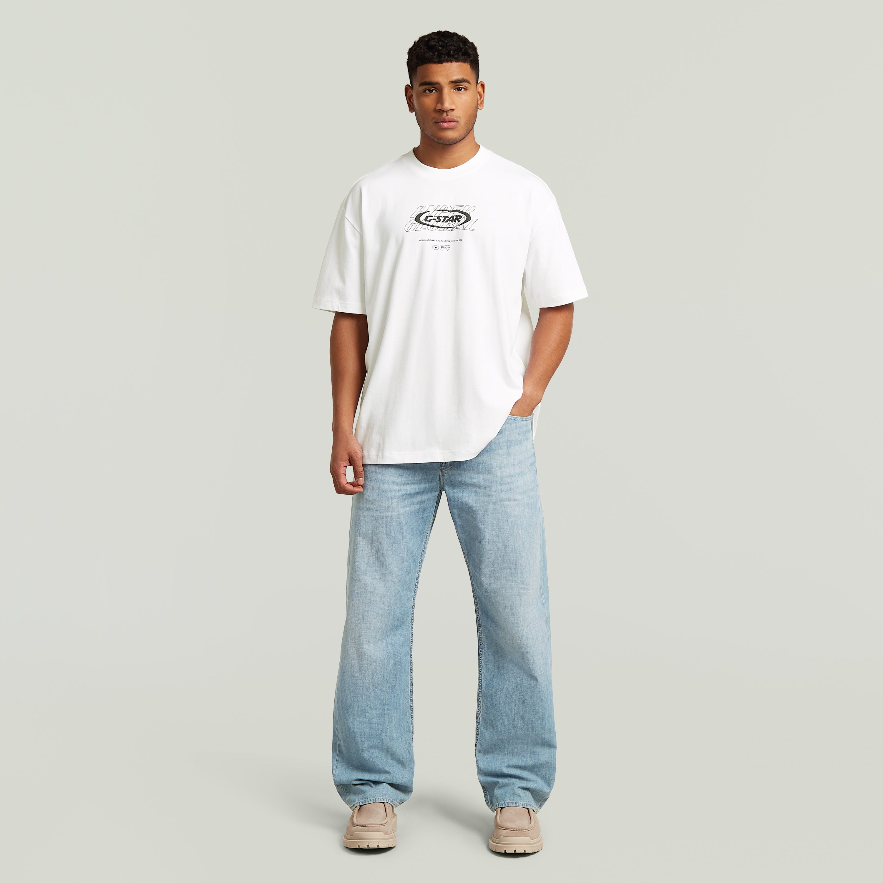 Model wearing a relaxed graphic t-shirt in white with relaxed fit and graphic print, styled with light blue jeans.