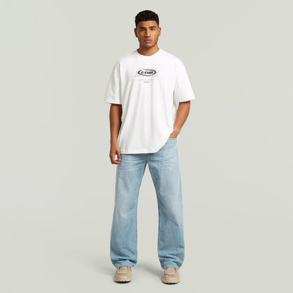 Model wearing a relaxed graphic t-shirt in white with relaxed fit and graphic print, styled with light blue jeans.