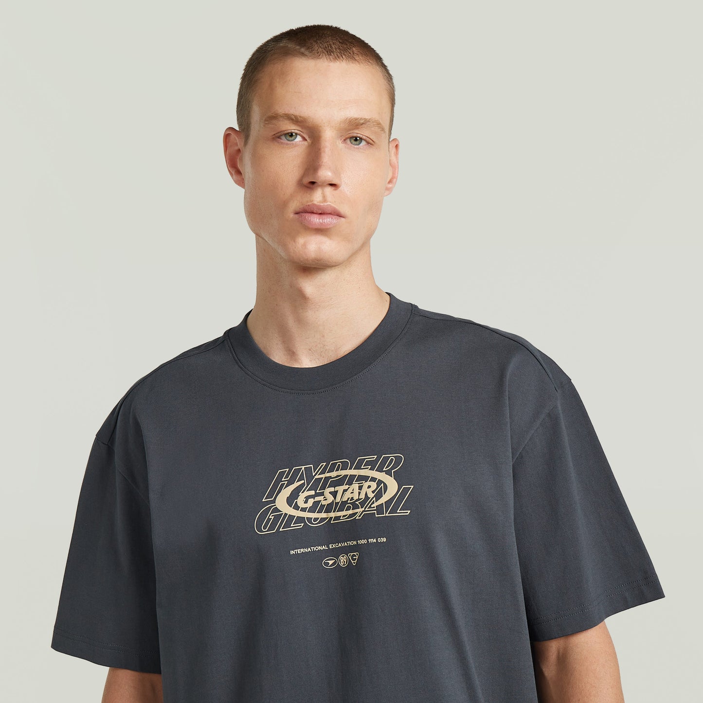 Modelo luciendo una camiseta Hyper Graphic Relaxed, relaxed fit graphic t-shirt color gris con estampado en el pecho.