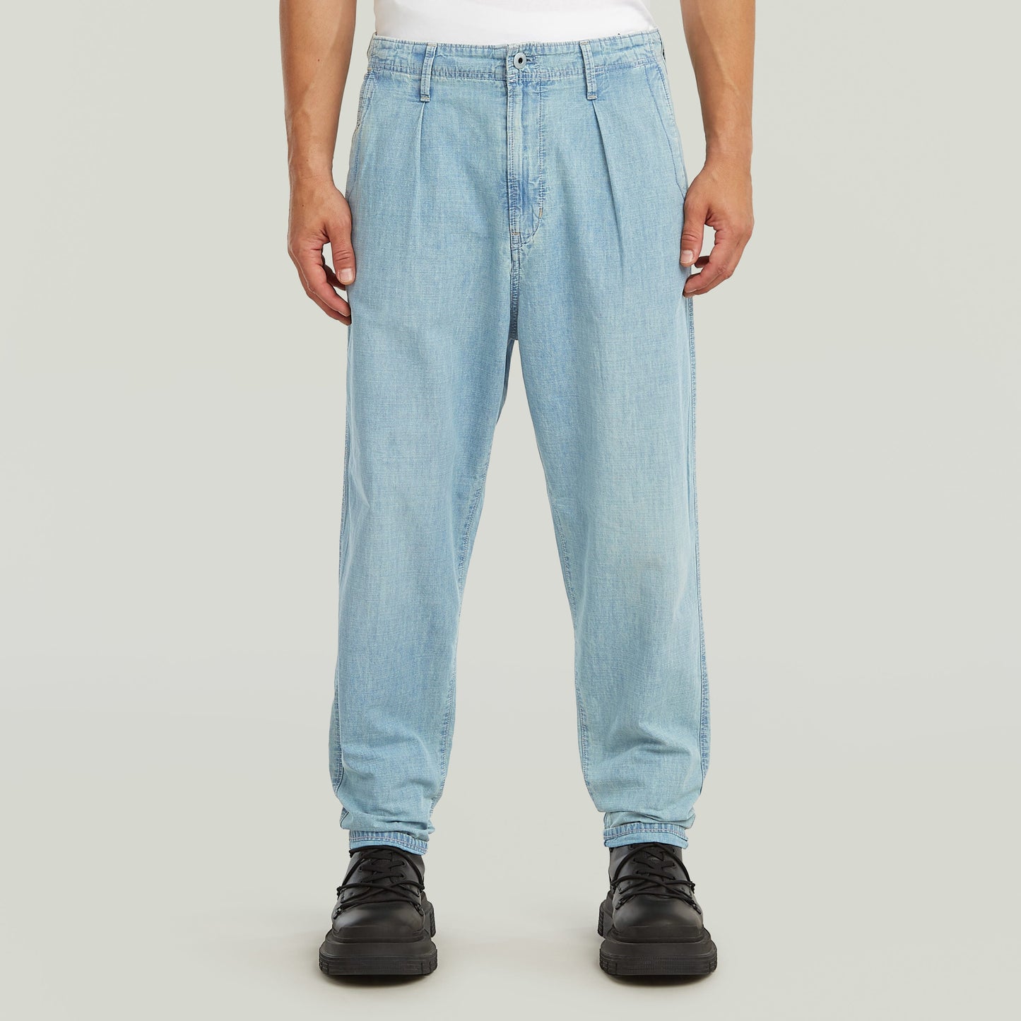 Denim relaxed tapered chinos with pleats and a relaxed fit, featured on a model.