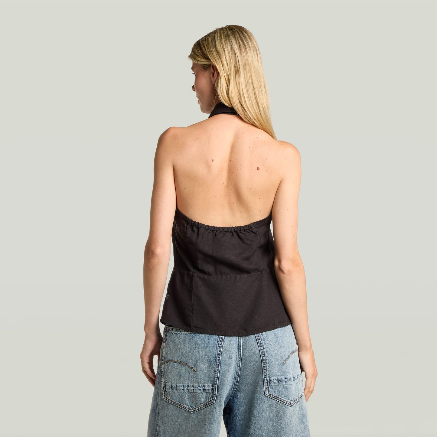Mujer de espaldas vistiendo el top halter fluid ligero en color negro, con pantalones de mezclilla.
