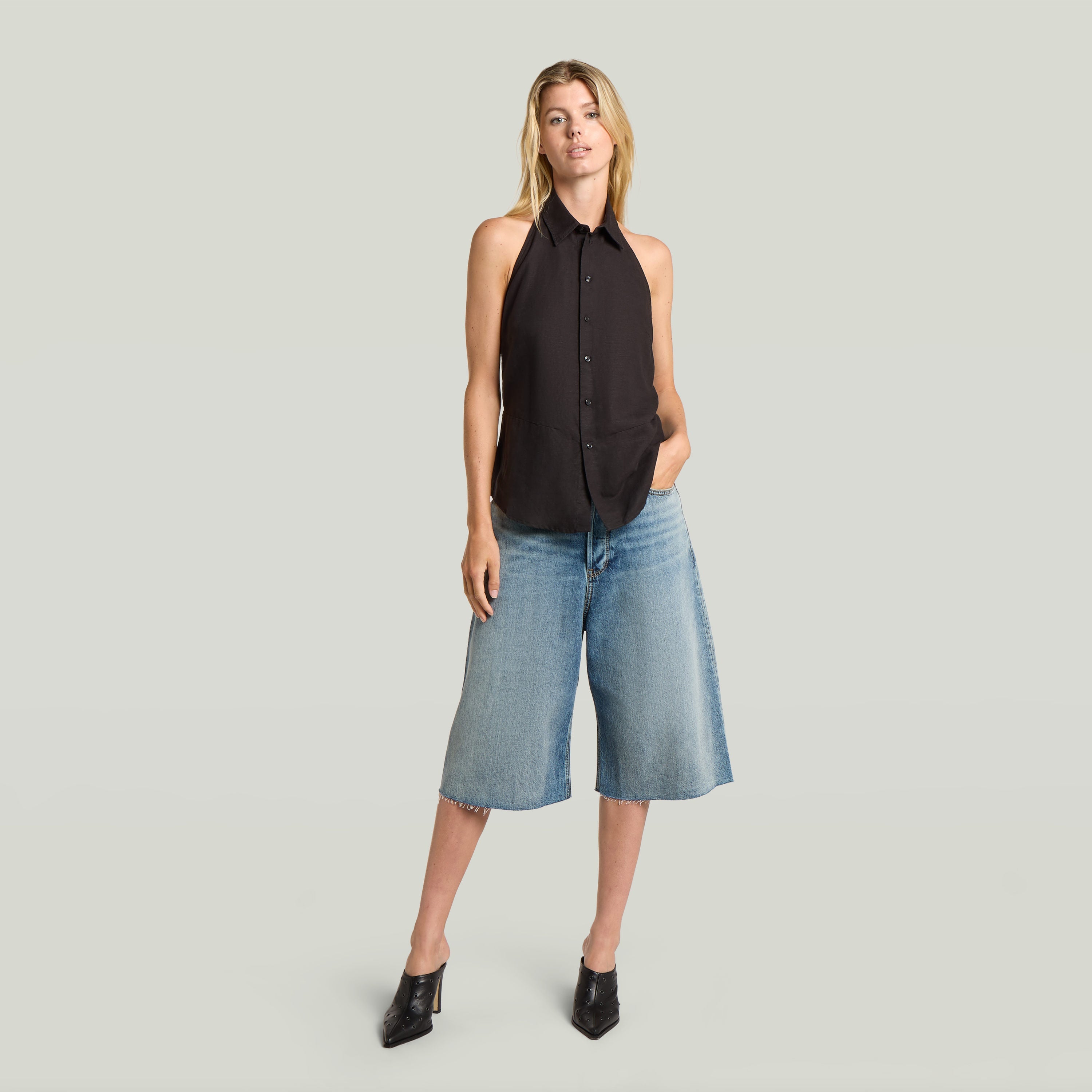 Mujer con un top halter negro sin mangas y pantalones de mezclilla cortos, mostrando un estilo moderno y ligero, halter neck top lightweight.