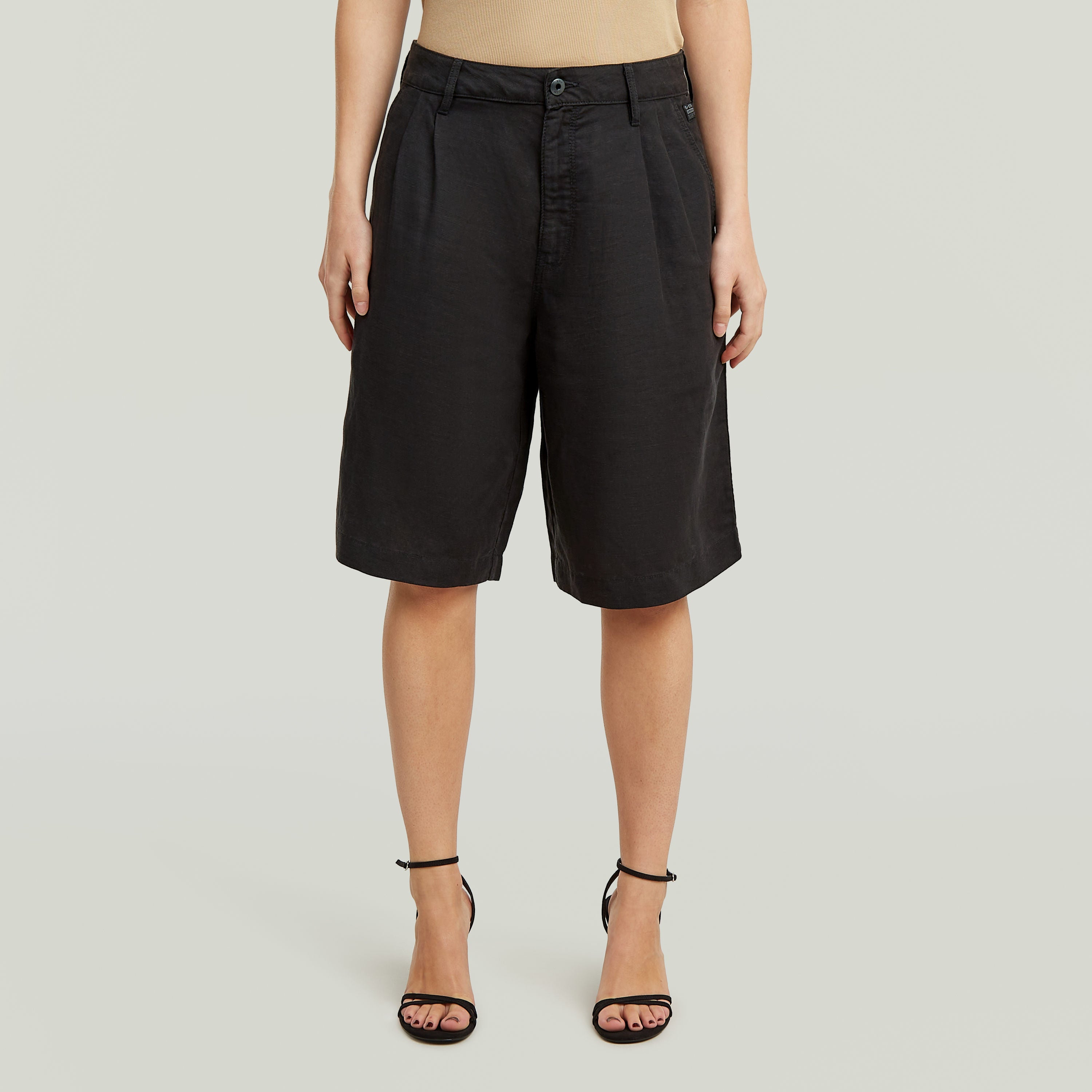 Mujer usando pantalón corto Pleated Bermuda negro, con cintura alta y diseño clásico plisado.