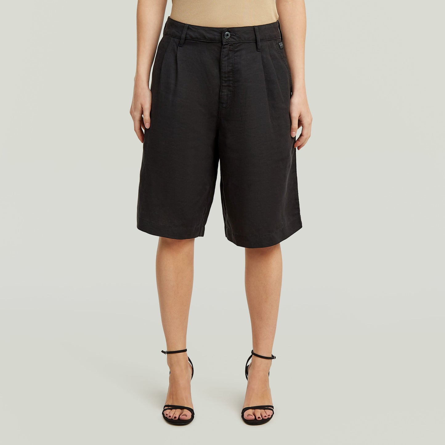 Mujer usando pantalón corto Pleated Bermuda negro, con cintura alta y diseño clásico plisado.