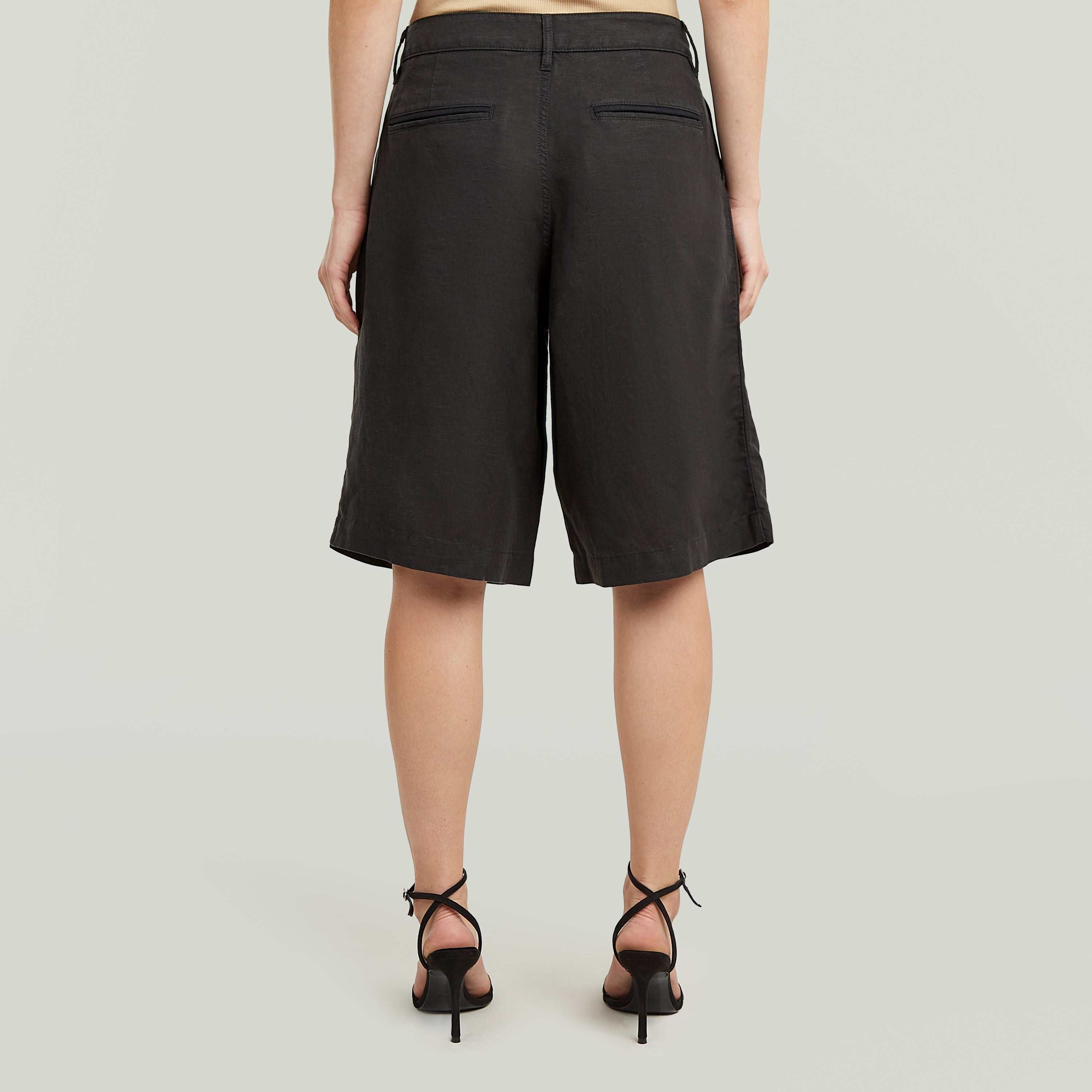 Mujer vista de espaldas luciendo shorts pleated bermuda color negro con diseño plisado y bolsillos.