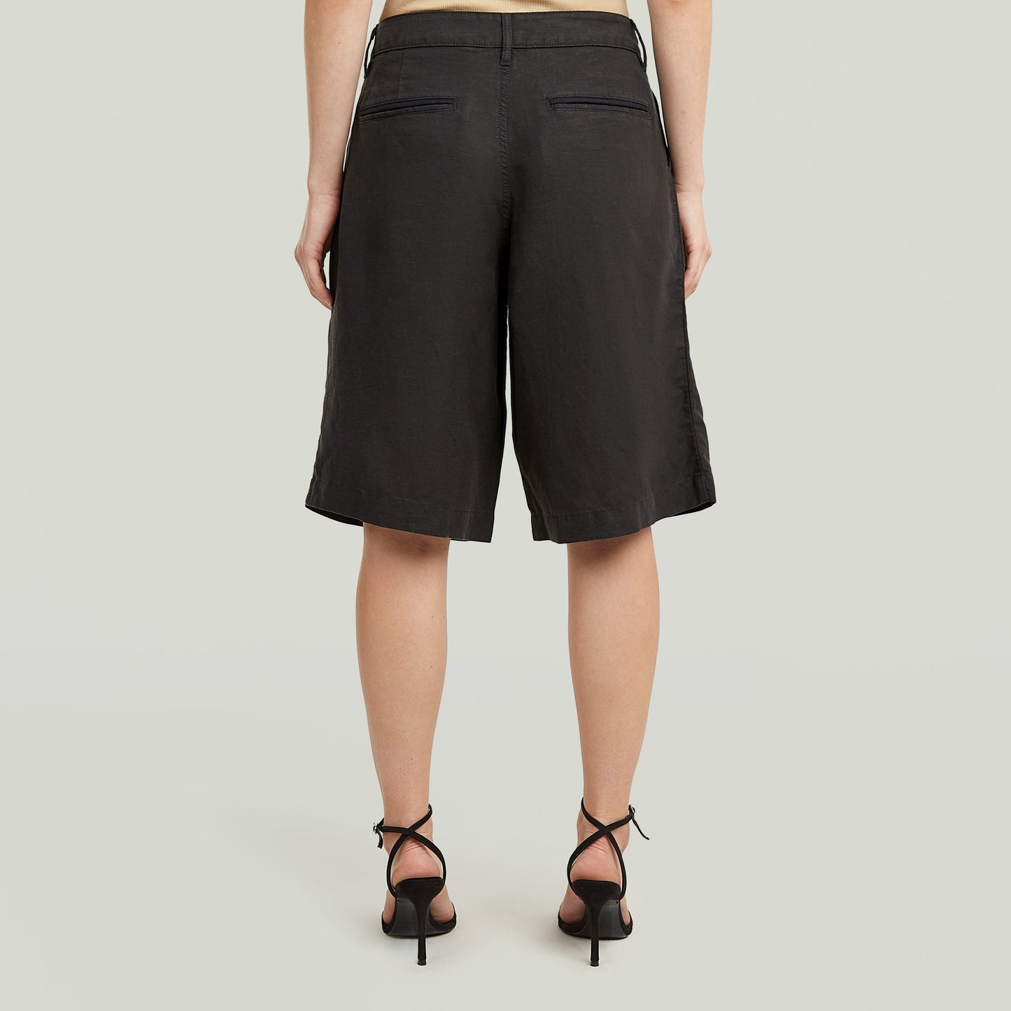 Mujer vista de espaldas luciendo shorts pleated bermuda color negro con diseño plisado y bolsillos.