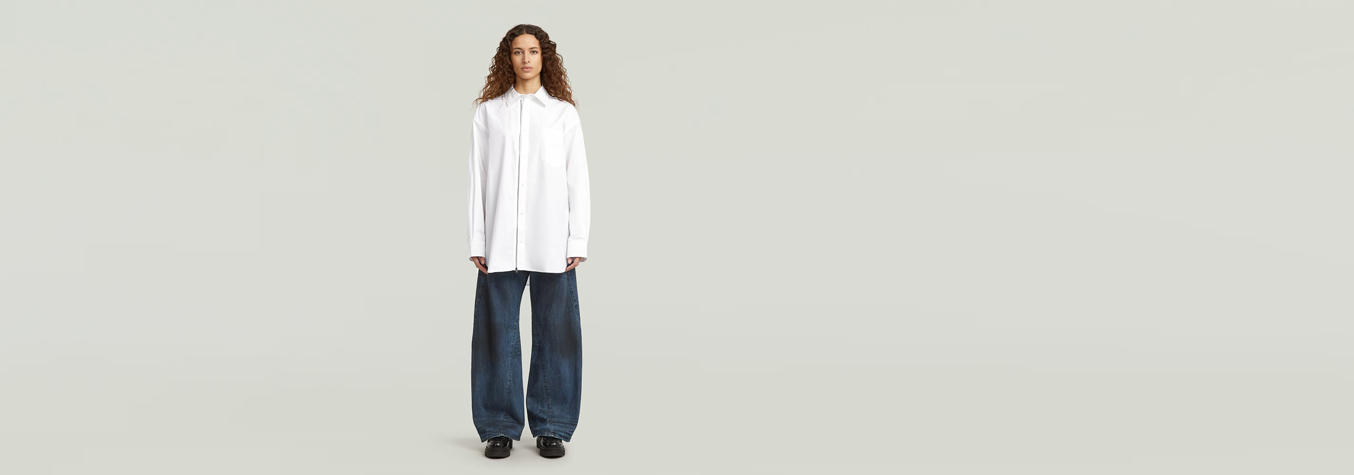 Modelo luciendo una camisa extragrande de popelín con cremallera sobre pantalones anchos.