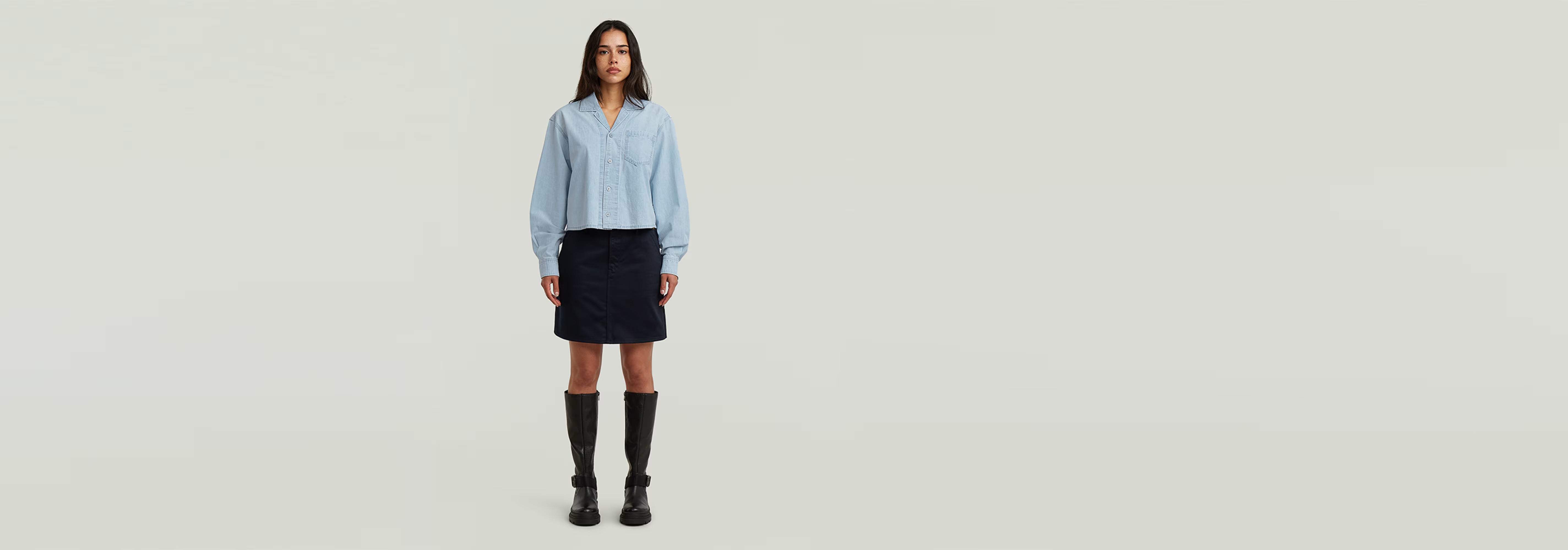 Mujer usando la Camisa Resort Boxy Relaxed con falda negra y botas altas en fondo claro.