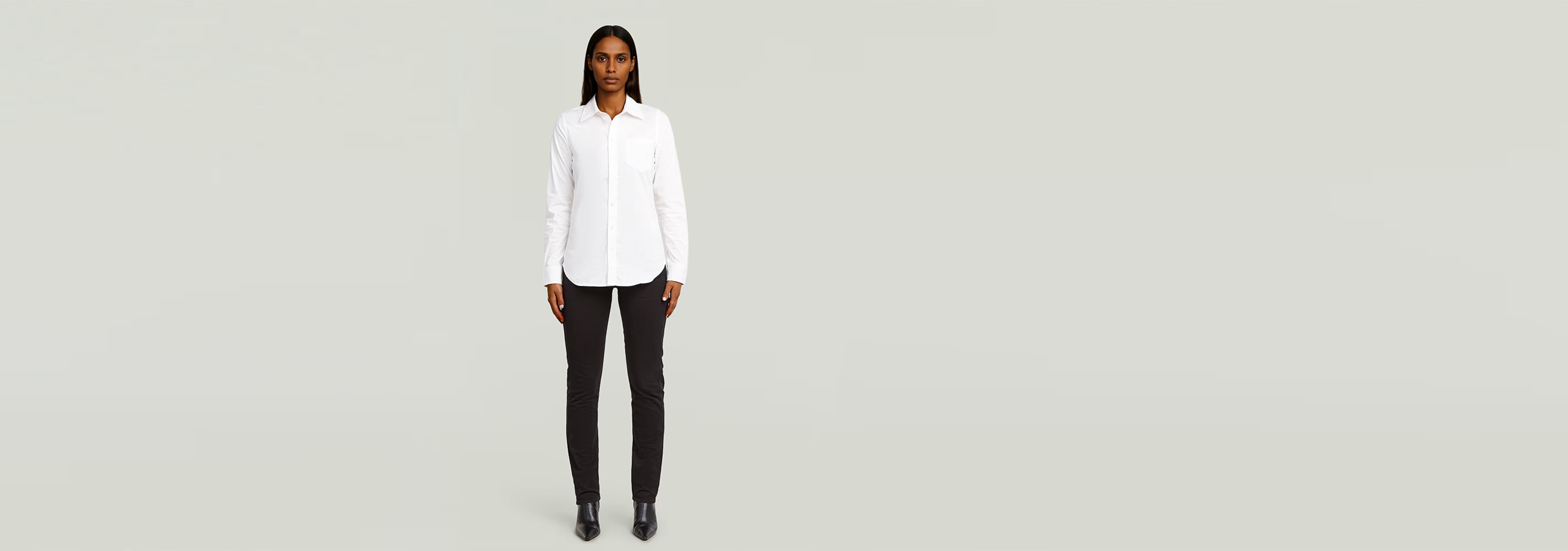 Modelo usando una Camisa Slim Poplin Long Sleeve blanca y pantalones negros en fondo claro.