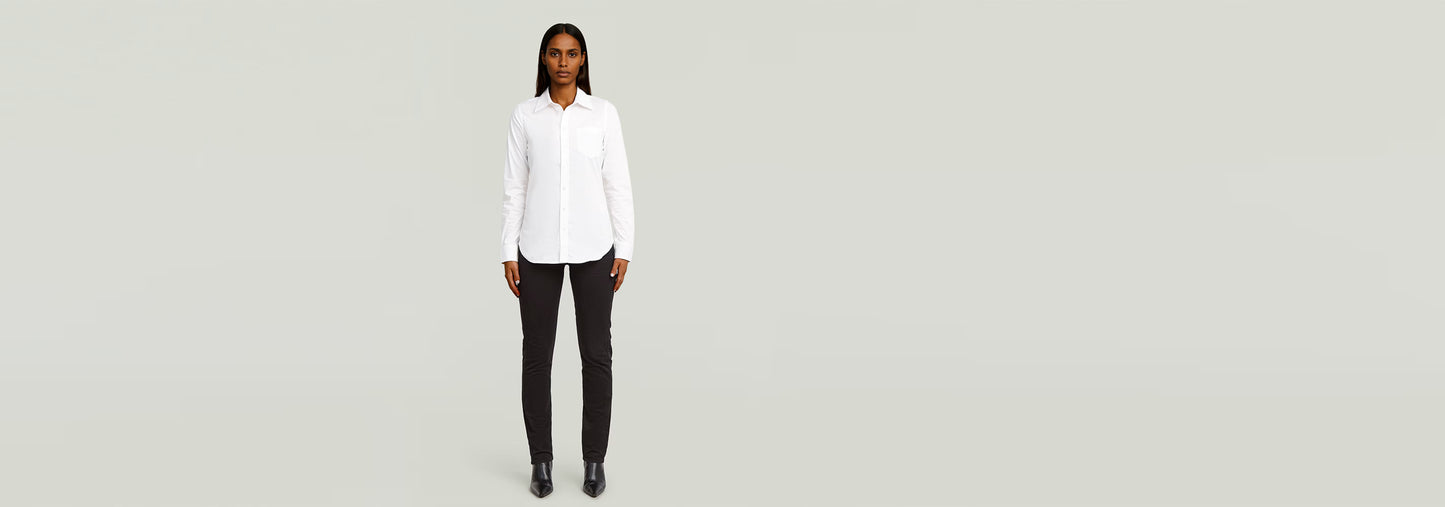 Modelo usando una Camisa Slim Poplin Long Sleeve blanca y pantalones negros en fondo claro.
