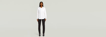 Modelo usando una Camisa Slim Poplin Long Sleeve blanca y pantalones negros en fondo claro.