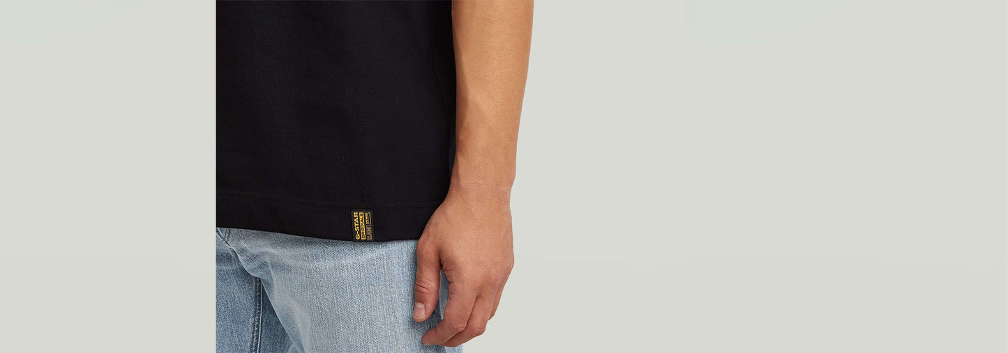 Camiseta GS-01 detalle del corte regular y logotipo sutil en el bajo, modelo usando pantalones claros.
