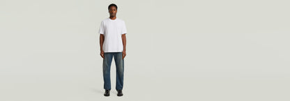 Hombre usando una camiseta GS-01 Relaxed blanca, con jeans, fondo gris claro.
