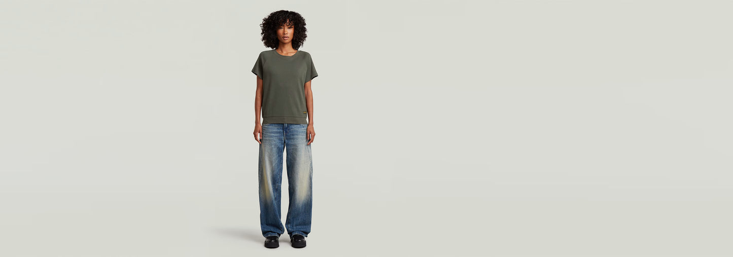 Mujer usando una camiseta Raglan de corte recto y jeans cómodos, fondo claro.