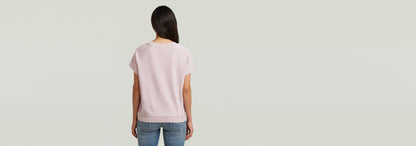 Mujer de espaldas luciendo camiseta raglan rosa, con corte recto y mangas de casquillo.
