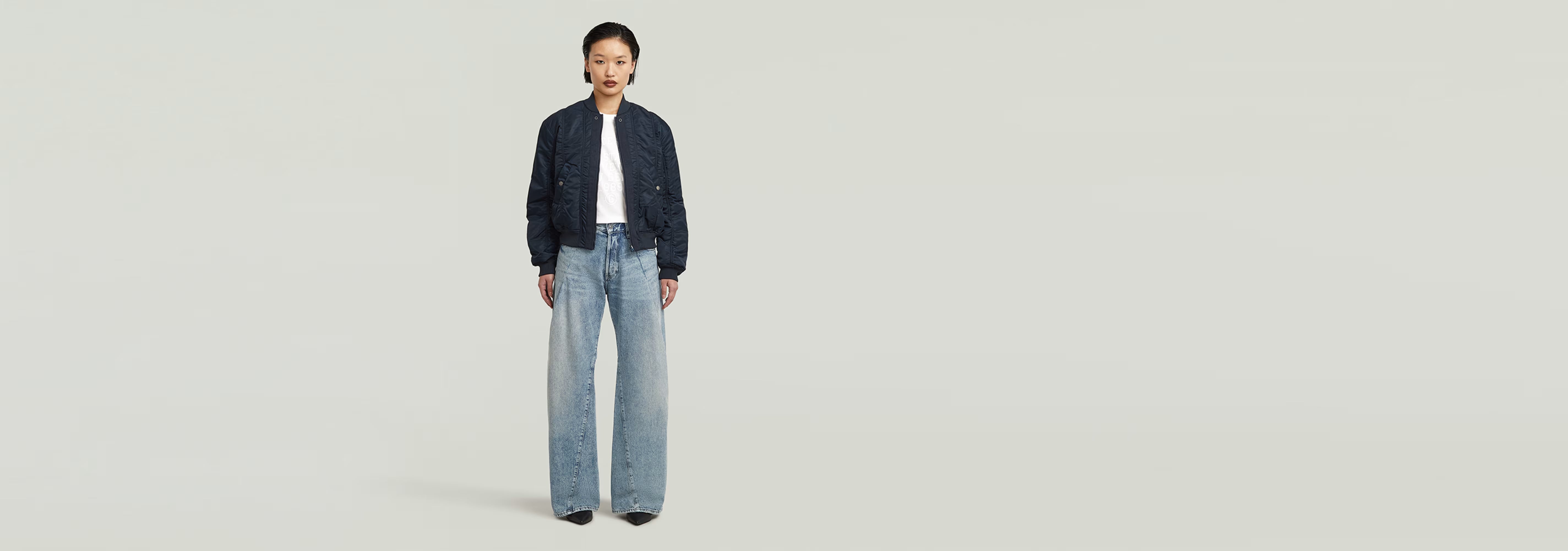 Mujer usando una cazadora de aviador con jeans anchos, fondo limpio y minimalista.