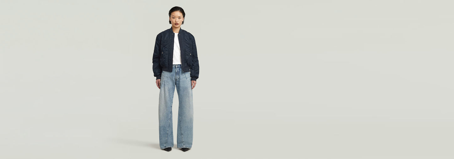 Mujer usando una cazadora de aviador con jeans anchos, fondo limpio y minimalista.